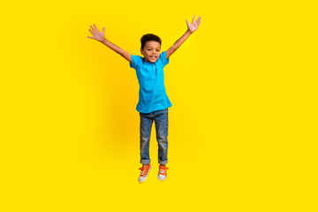 Fototapeta na wymiar Full body photo of positive cute small child dressed blue t-shirt jeans flying raising arms up isolated on vibrant yellow background
