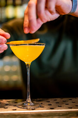 A skilled bartender garnishing a bright yellow cocktail in a martini glass, showcasing the elegance of mixology