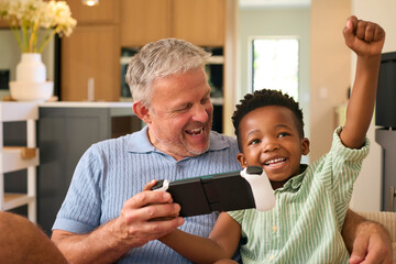 Multi Racial Family With Grandfather And Grandson Playing On Handheld Gaming Device Together - obrazy, fototapety, plakaty