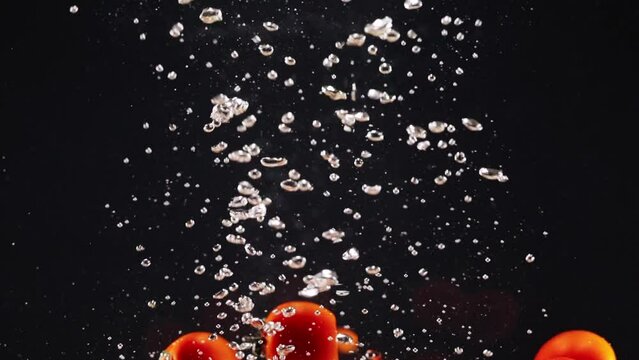 Fresh red tomato dropping in water and splashing isolate on black background