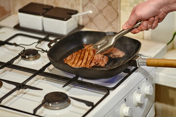 The process of cooking two beef steaks in frying pan, the hands of male chef salting raw meat,...
