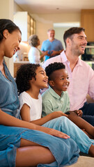 Family Laughing Sitting On Sofa Watching TV At Home With Grandparents In Background