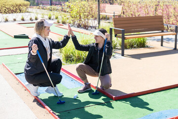 mother and daughter playing mini golf, children enjoying summer vacation - 792751967