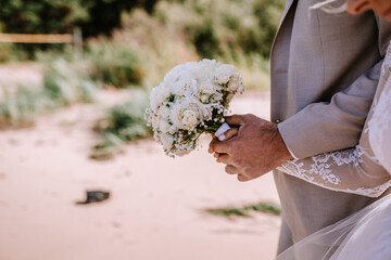 Valmiera, Latvia - August 10, 2023 - Close-up of a groom holding a bridal bouquet of white roses at...
