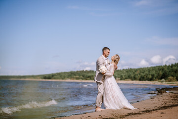 Valmiera, Latvia - August 10, 2023 - Bride and groom embracing on the beach, waves gently breaking...