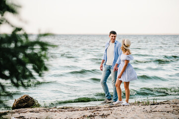 Female and male walk on beach and enjoying summer day. Happy man and woman walking on sand sea. Side view. Couple in love holding hands and looking at each other on seashore. Spending time together.