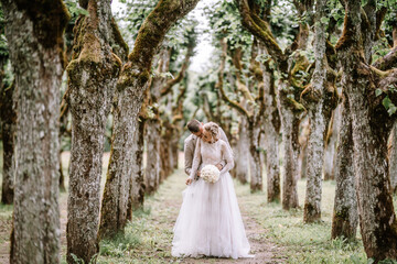 Valmiera, Latvia - August 10, 2023 - A wedding couple embracing among a moss-covered avenue of...