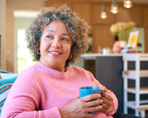Mature Woman Sitting On Sofa At Home Relaxing With Hot Drink