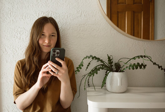 Woman scrolls on phone while sitting in minimal interior space
