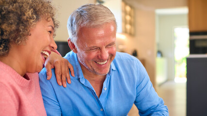 Loving Multi-Racial Mature Couple Sitting On Sofa At Home Laughing And Talking Together