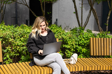 Young woman sitting on online meeting in outdoor cafe, talking to laptop camera, explaining something, drinking coffee.