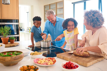 Obraz na płótnie Canvas Grandchildren Helping Grandparents Prepare Meal In Kitchen At Home Having Messy Fun Together