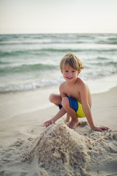 Smiling boy with sandcastle on a sunny beach