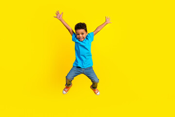 Full size photo of overjoyed little schoolboy wear blue t-shirt denim pants raising palms jumping...