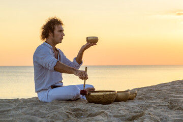 Young man meditating sound OM with tibetan singing bowl on sunset