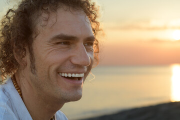 Portrait of smiling curly-haired man on sea on sunset, close up