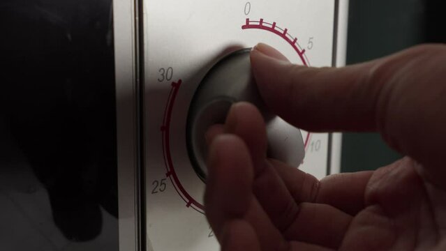 Hand Turning Off Microwave Oven Timer Control Knob. closeup shot