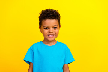 Photo of adorable positive good mood kid with curly hair dressed blue t-shirt toothy smiling...