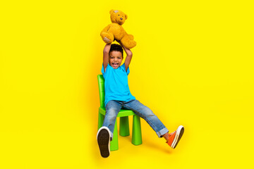 Full body photo of overjoyed small child dressed blue t-shirt raising up teddy bear over head...