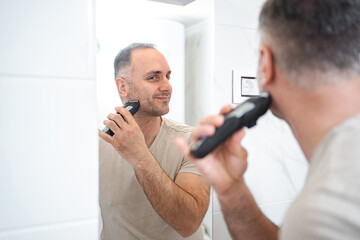 Man shaves his beard with a trimmer in the bathroom
