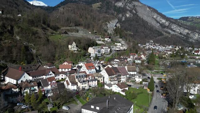 Drone clip showing traditional white buildings in Swiss Alps, next to calm lake, on sunny day in Springtime
