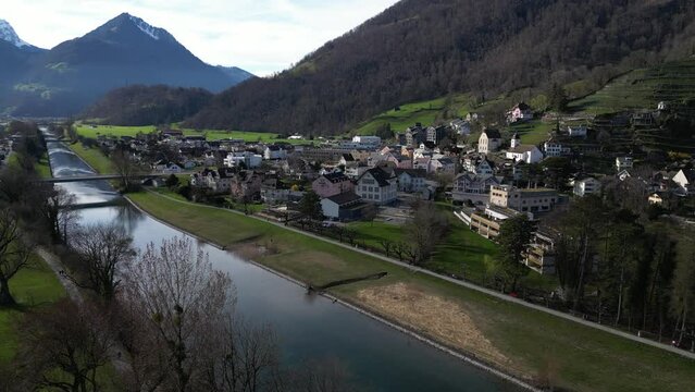 Drone clip of calm river next to traditional Swiss village in Alps