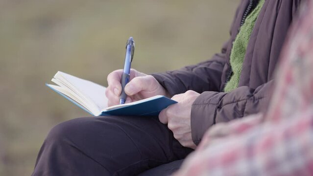 Elderly woman takes notes in journal during group therapy session, shallow focus