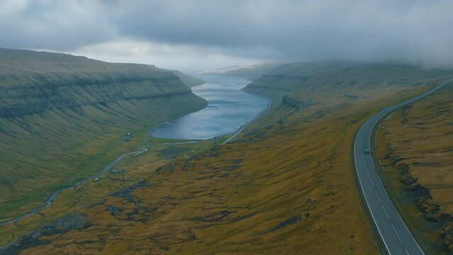 Scenic Road Trip: Aerial Views of Car Followed by Drone Capturing Stunning Faroe Islands Landscape.