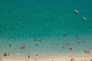 Aerial view of sandy beach with swimming people in sea with transparent blue water in summer.