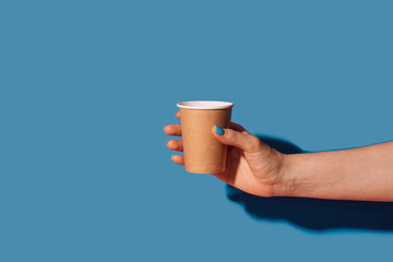 Paper cup with takeaway coffee in female hand against blue background.