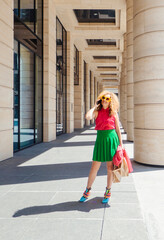 Content fashion female with bag walking on pavement near stone columns in sunlight and talk cell phone. the concept of freedom of tourism and fashion business