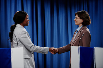 Side view of two intercultural female delegates or political leaders shaking hands and looking at...