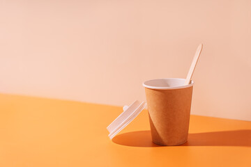 Empty paper cup with wooden spoon on beige background.