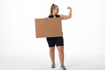 Plus size Caucasian woman shows strong arm, holds sign on white background, copy space