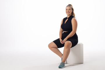 A young Caucasian plus-size model sits on white block with a white background, copy space - 792789528