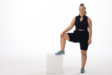 A young Caucasian plus-size model stands with one foot on white box, copy space