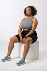Biracial young female plus size model sits on white background, copy space