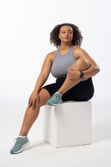 Biracial plus size model with curly hair holds leg on white background, copy space - 792789569