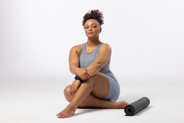 Biracial young female plus size model sits next to yoga mat on a white background, copy space - 792789727
