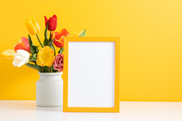 Festive floral background. Beautiful tulip flowers and yellow empty photo frame on yellow  background. 