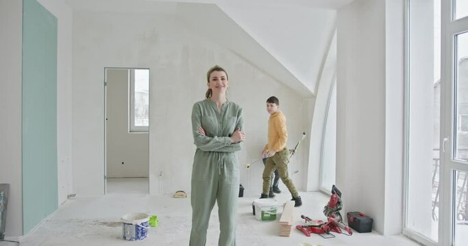 A joyful family of three engages in a DIY home renovation project, painting the walls of their new apartment. Mother smiling broadly, with her two sons actively painting the walls, reflecting teamwork