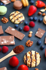 Fototapeta na wymiar Macarons, chocolate, cookies, berries and various nuts on dark blue background. Selective focus.