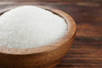 Granulated sugar in bowl on wooden table, closeup