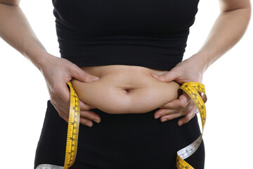 Woman with measuring tape touching belly fat on white background, closeup. Overweight problem