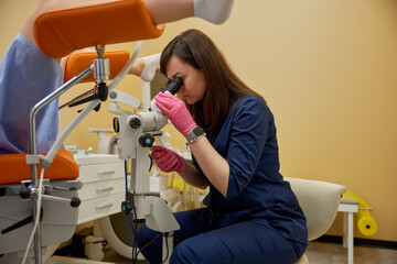 Gynecologist looking in colposcope examining patient on disease
