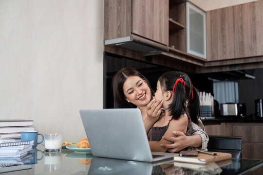 Working mom work from home office. Happy mother and daughter look to each other. businesswoman and cute child using laptop work freelancer workplace in living room