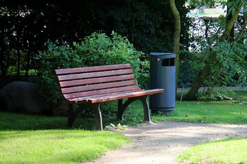 Beautiful wooden bench stands next to a metal trash can in a park