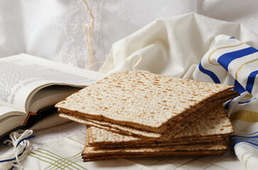 Stack of matzah, a book, and a tallit. The matzo is in the foreground. Adjacent to it lies an open book Tora. The setting appears serene and peaceful, religious traditional Jewish setting passover