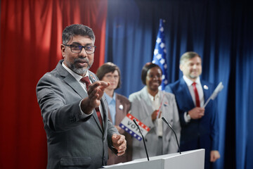 Confident multiethnic male politician in formalwear making speech during voting campaign while...