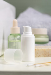 White pump cream bottle near soap, green cosmetic bottles and jars in bathroom, mockup